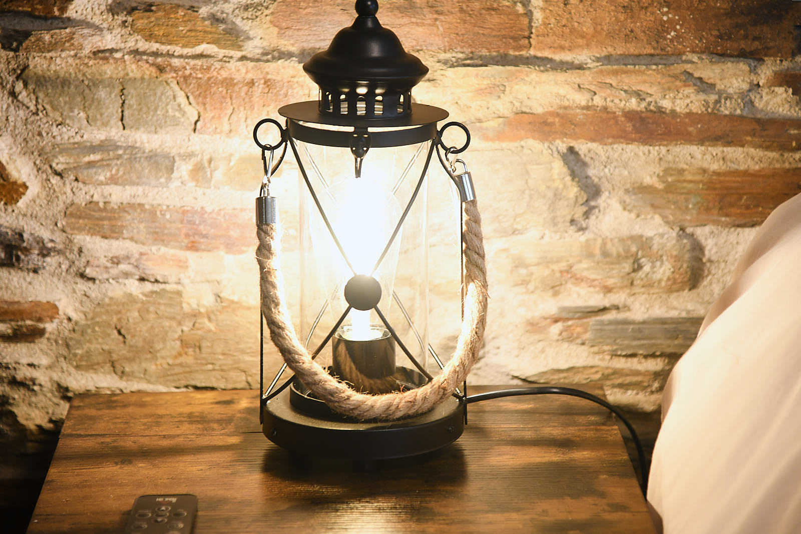 Black metal lantern glowing beside a wooden bedside cabinet