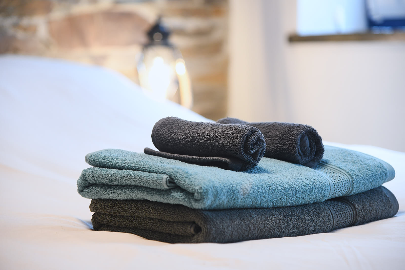 Folded blue and charcoal towels with rolled hand towels on white bedding