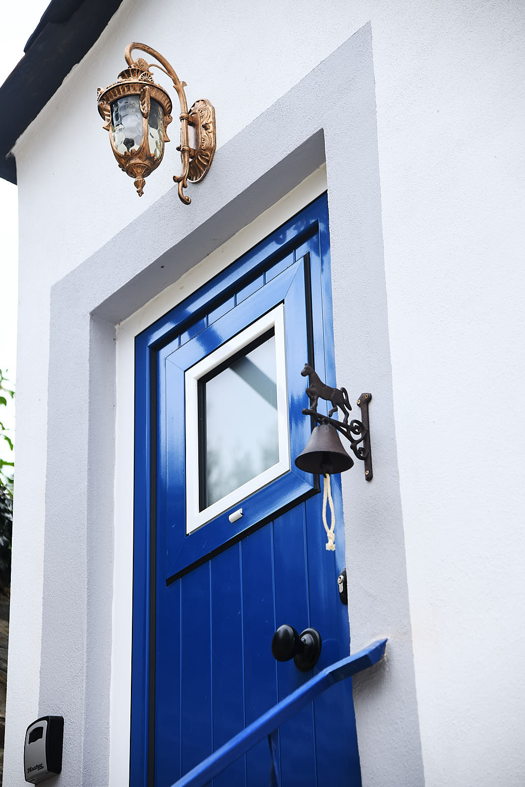 Casa da Égua blue entrance door with a bronze wall lantern and bell