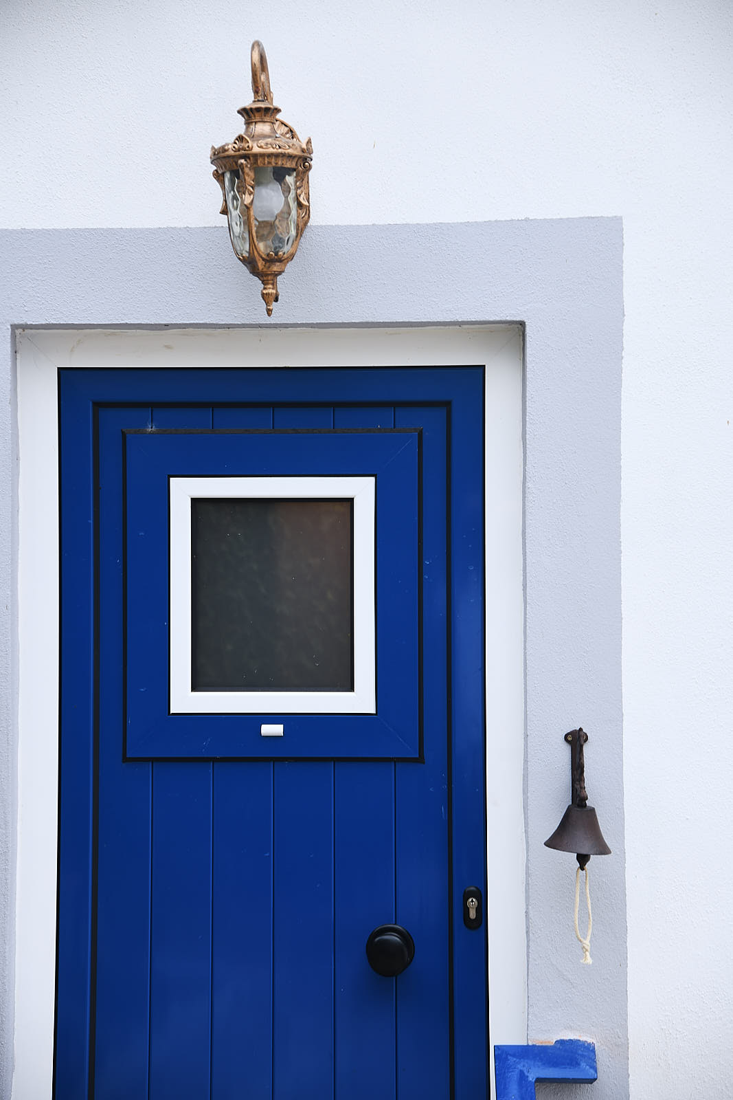 Close-up of the blue entrance door, bronze lantern and bell