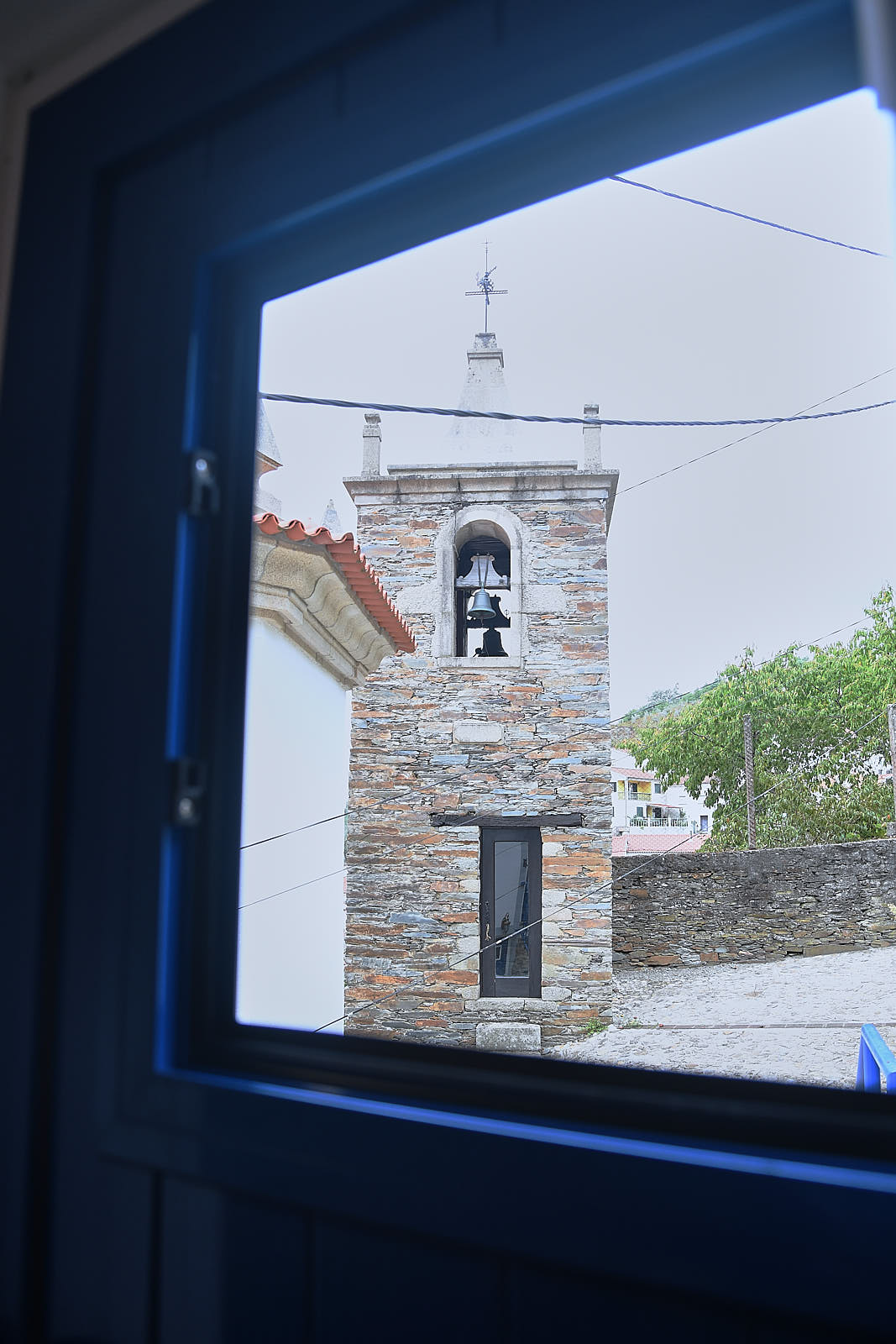 View of Benfeita's stone bell tower through a blue Casa da Égua window